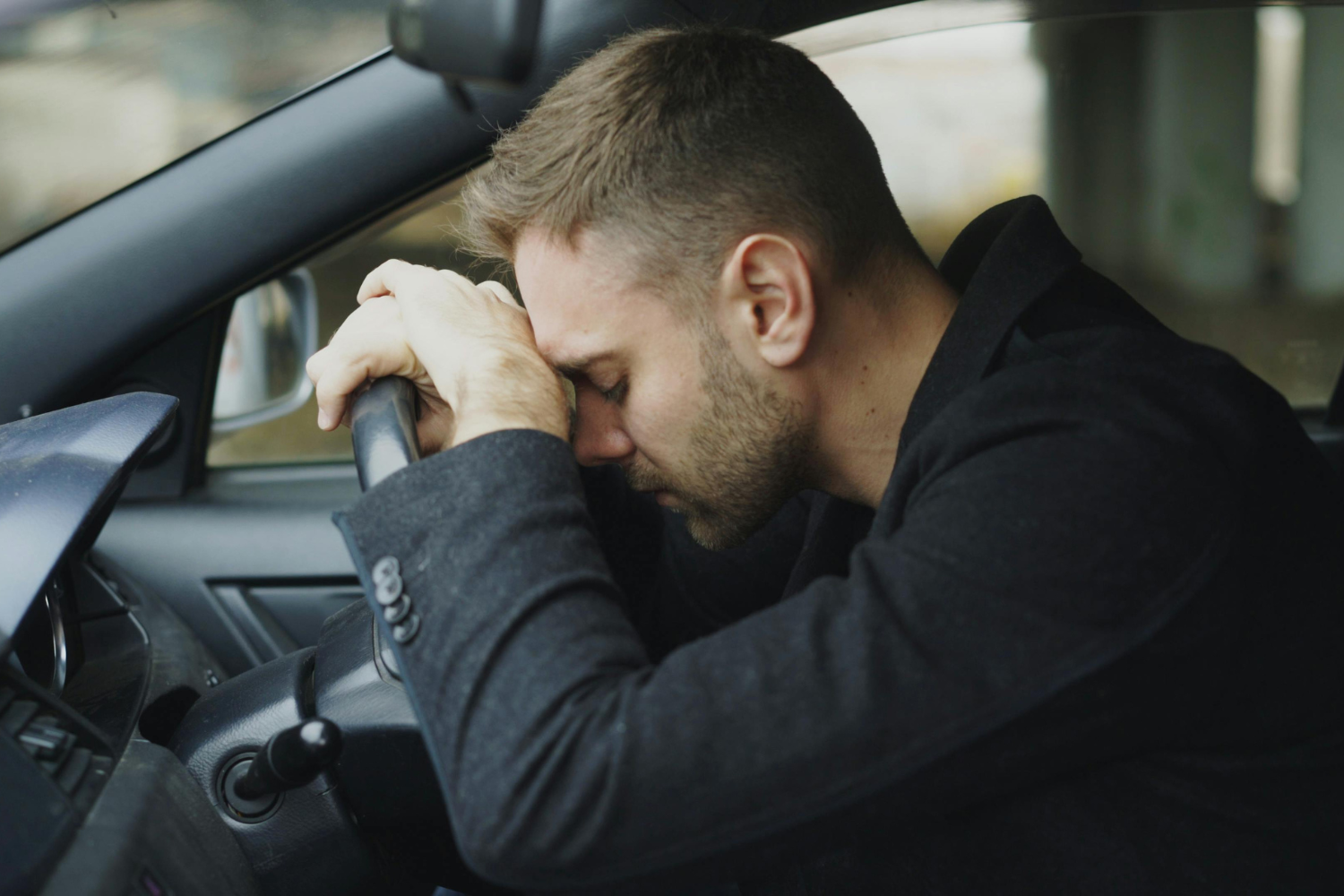 Motorista com a mão no volante e a cabeça baixa dentro do carro, representando preocupação com problemas que podem causar a perda do seguro.